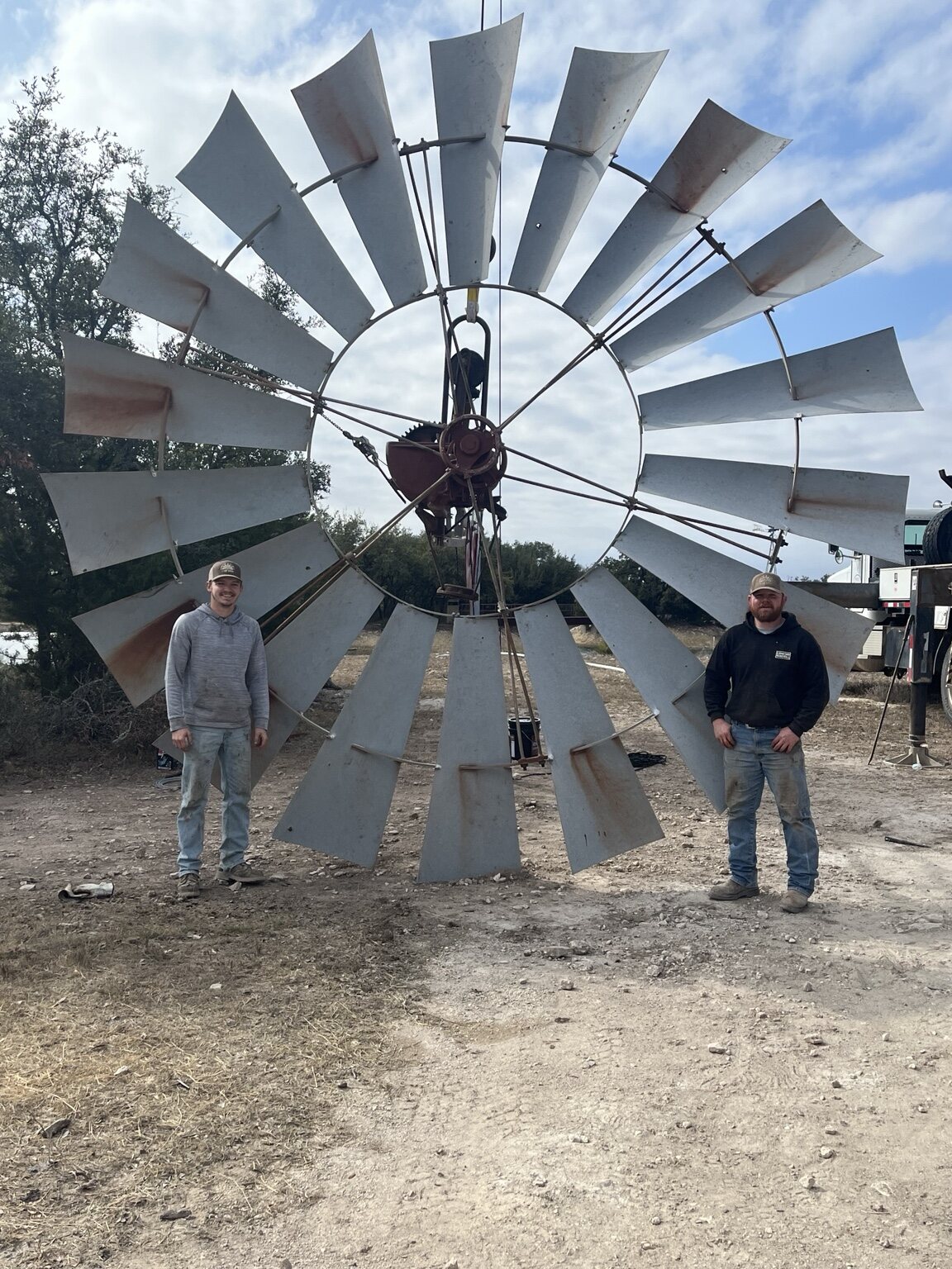 Two Concho Windmill crew members standing beside a large windmill wheel